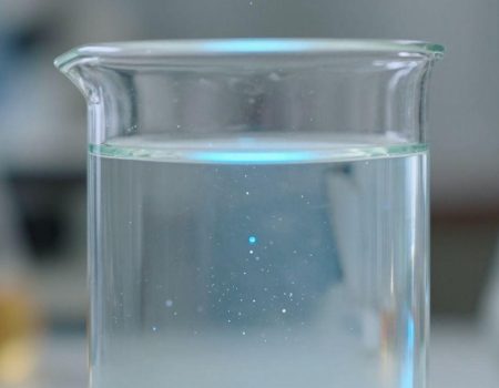 Laboratory beaker with glowing liquid and particles.